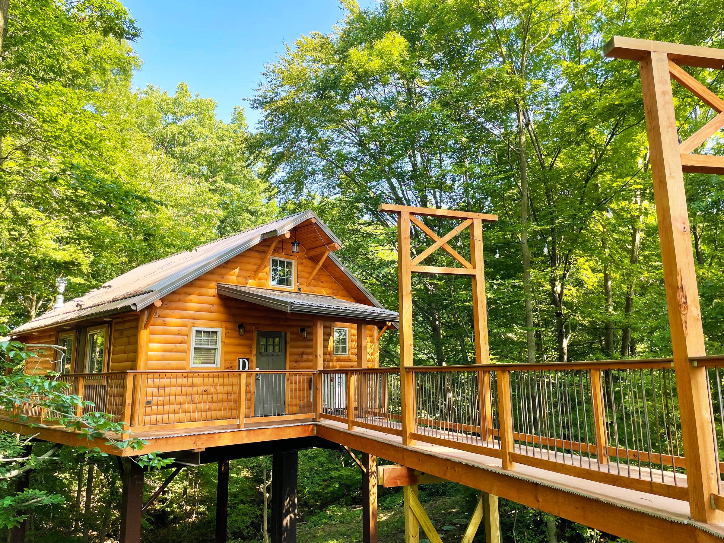 Exterior of Cricket Hill Treehouse D on stilts among the trees with its walkway bridge in Berlin, Ohio